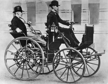 Gottlieb Daimler in seiner Motorkutsche von 1886, dem ersten vierrädrigen Benzinautomobil der Welt, am Steuer Daimlers Sohn Adolf.